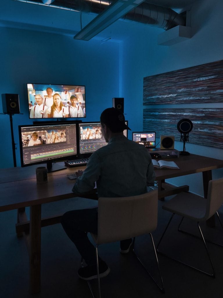 A video production editor sitting at a desk working on a professional editing suite.