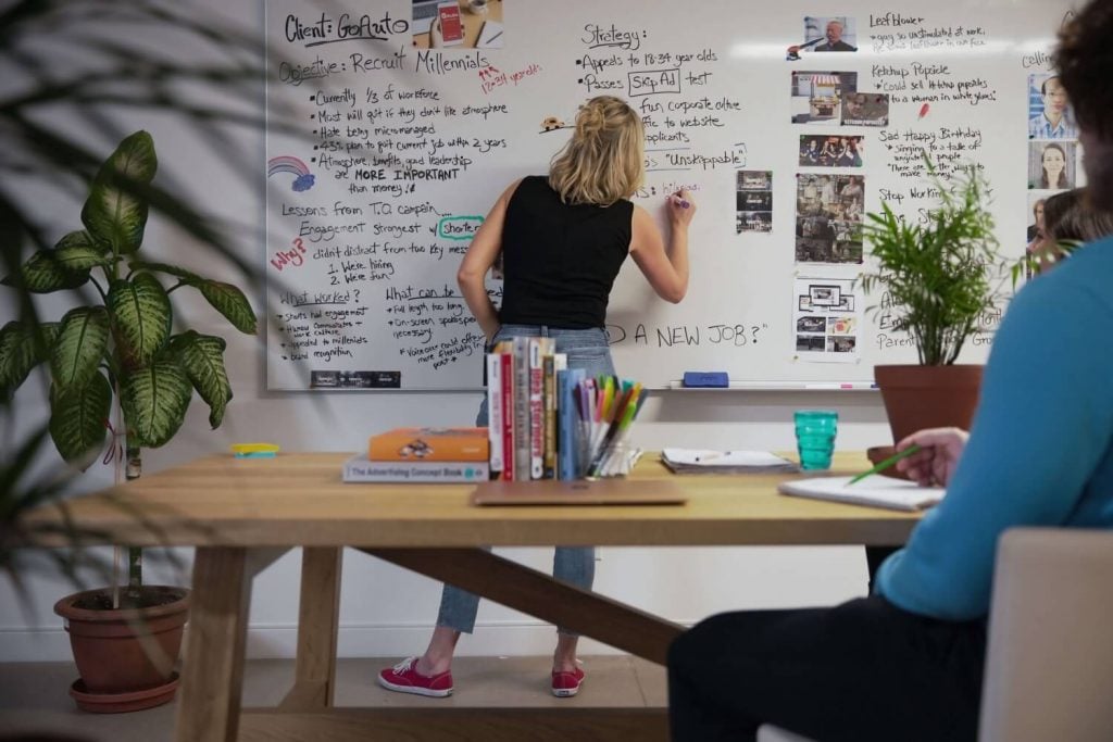 Female marketing agency employee in Edmonton writes on a whiteboard at a meeting.